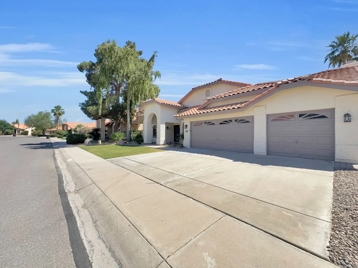 This image captures the home's front entrance, garage doors, and a beautifully landscaped yard, all under a clear sky. The scene conveys a welcoming arrival and hints at outdoor spaces suitable for gatherings and relaxation.