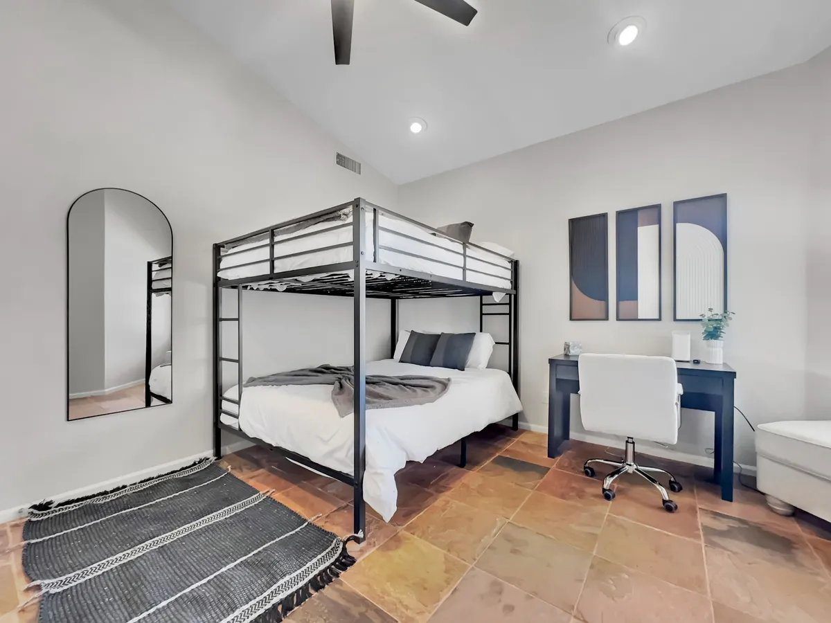 A modern, inviting bedroom with a bunk bed and a well-equipped desk and chair, complemented by a mirror and abstract wall art. The setup is ideal for both studying and working, with plenty of natural light and a functional yet cozy atmosphere.