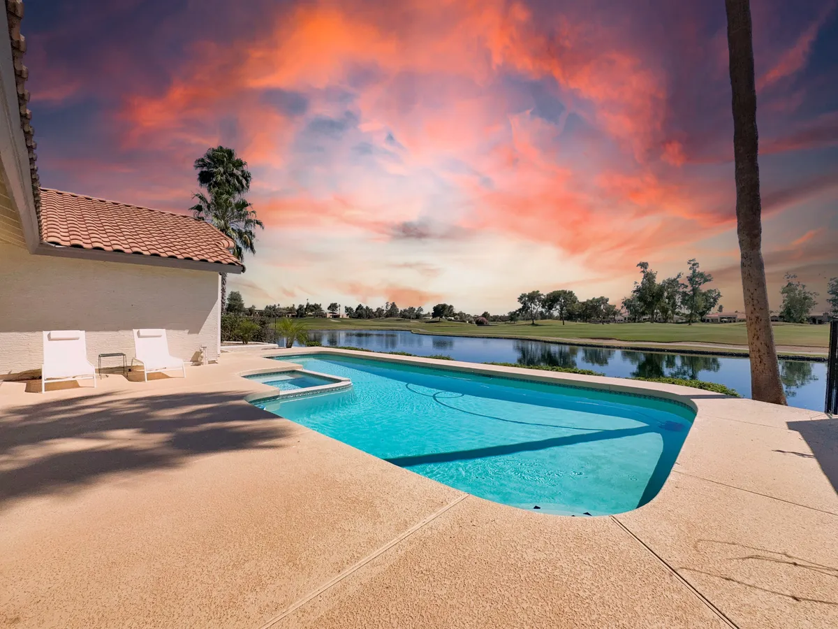 A serene outdoor pool scene featuring a sparkling swimming pool surrounded by lounge chairs, with the lake visible in the background and an open sky overhead. The setting suggests both relaxation and outdoor enjoyment in a tranquil waterfront environment.