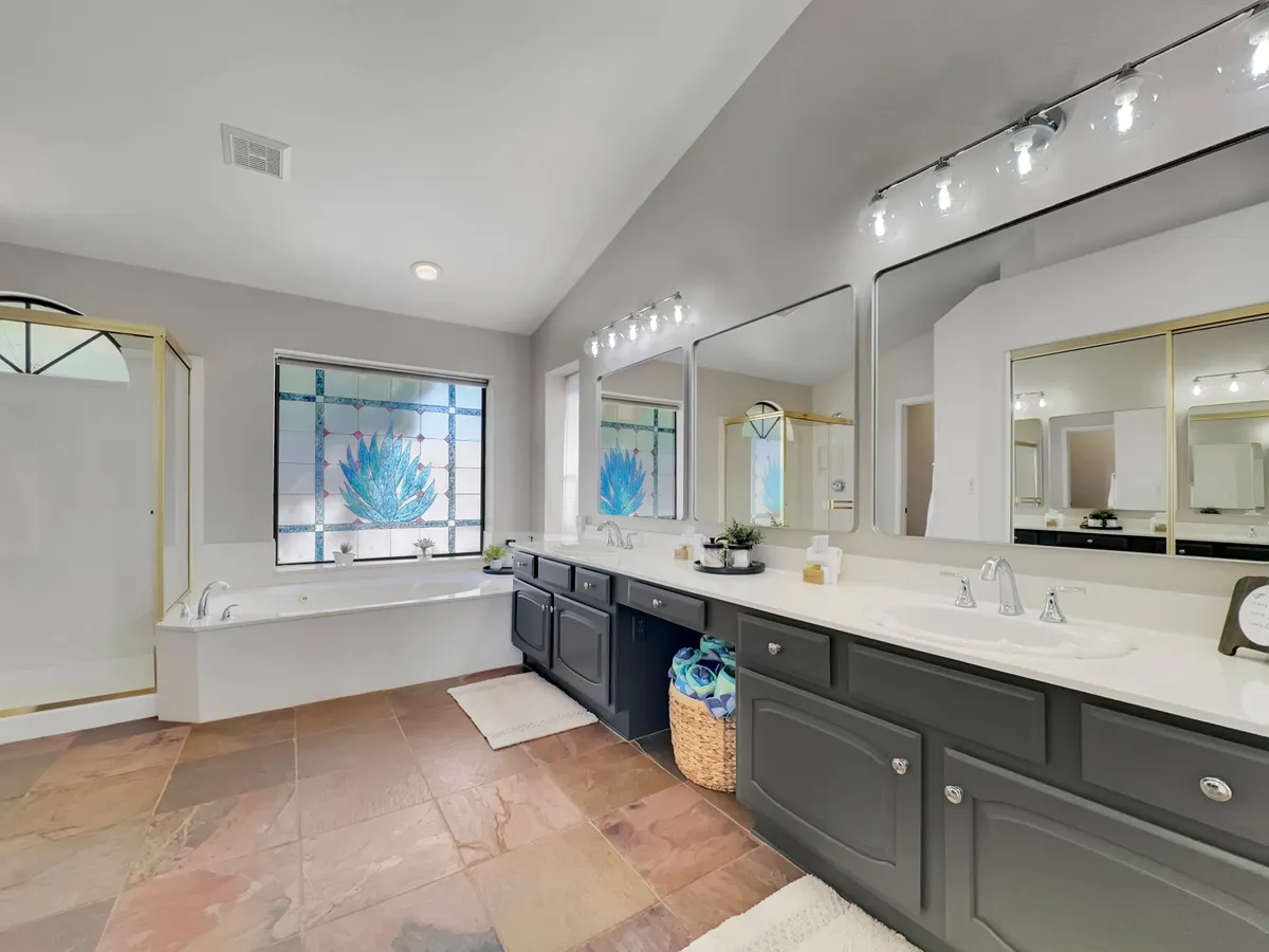 A spa-like bathroom with a striking stained glass window that allows natural light to filter in, a double sink vanity, a freestanding bathtub, and a sleek shower enclosure. The tranquil setting is designed for relaxation and self-care rituals, evoking a luxurious, rejuvenating ambiance.