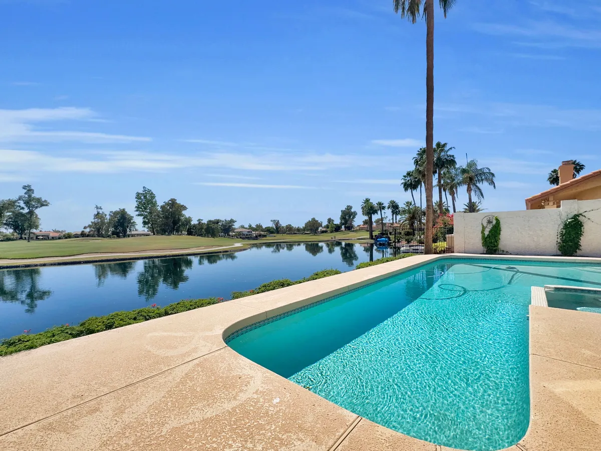 A serene backyard view featuring a sparkling swimming pool bordered by palm trees, with a striking vista of the adjacent golf course. The tranquil water reflects the sky, and the scene invites relaxation poolside while keeping the lush fairways in view.