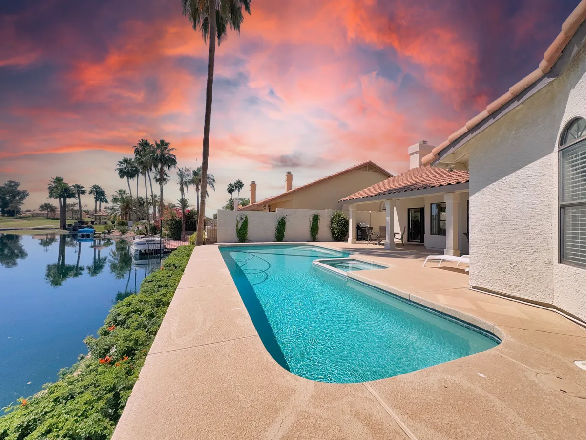 This exterior image showcases a stunning swimming pool surrounded by palm trees, with a picturesque lake view in the background beneath a glowing sunset sky. The luxurious setting includes the pool, lush landscaping, and a tranquil lake, evoking the essence of resort-style living and relaxation.