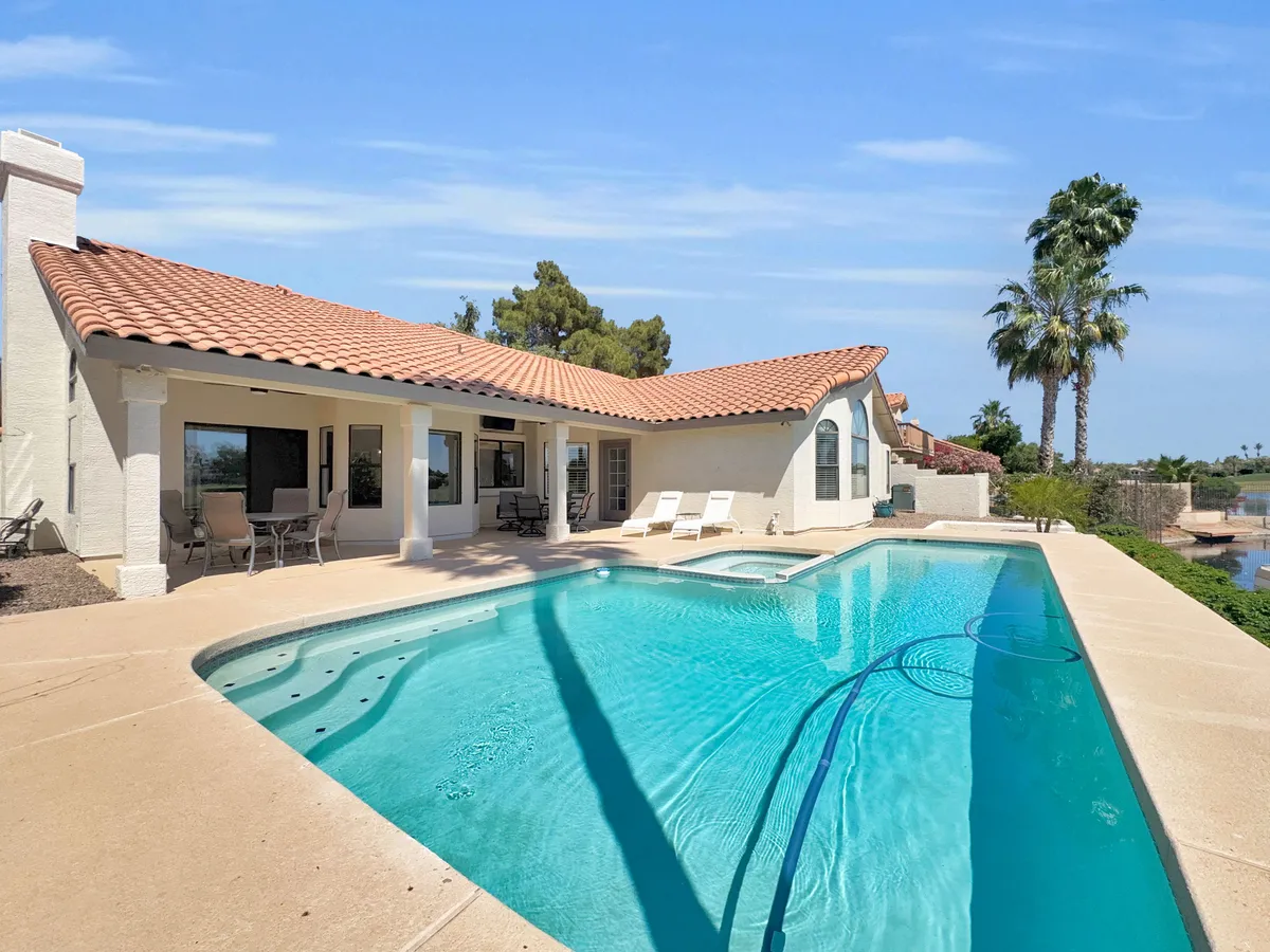 A welcoming outdoor space featuring a sparkling swimming pool, palm trees, ample seating, and part of the house’s exterior. The inviting atmosphere is perfect for outdoor dining, sunbathing, or gathering with the entire family after a day of fun.